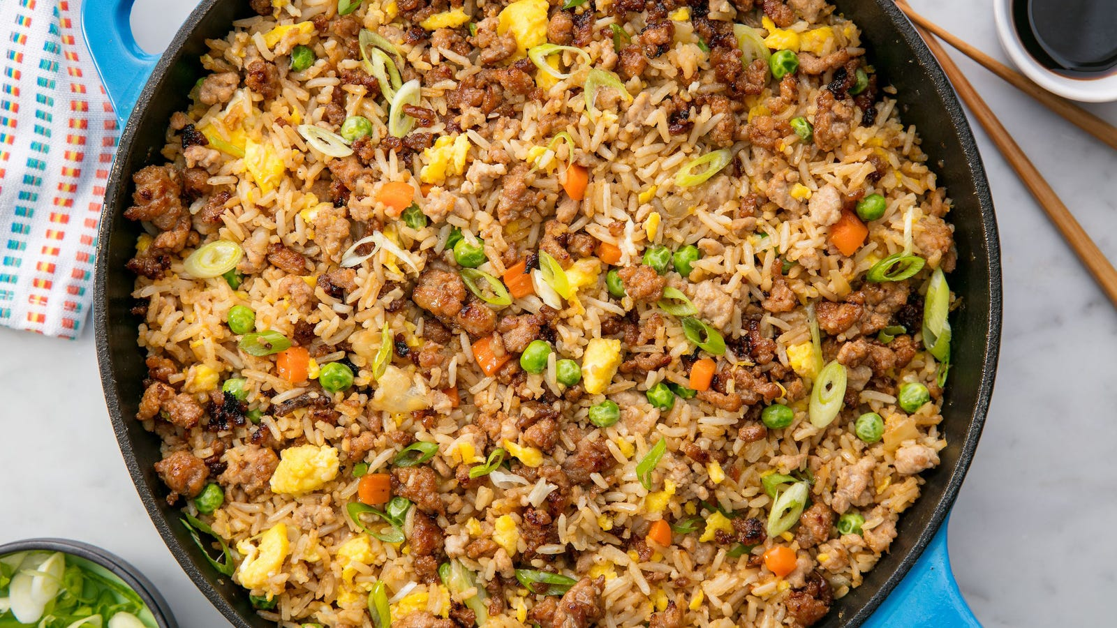 A large blue cast-iron pan of fried rice with browned pork mince, scrambled egg, peas, carrot and sliced spring onion
